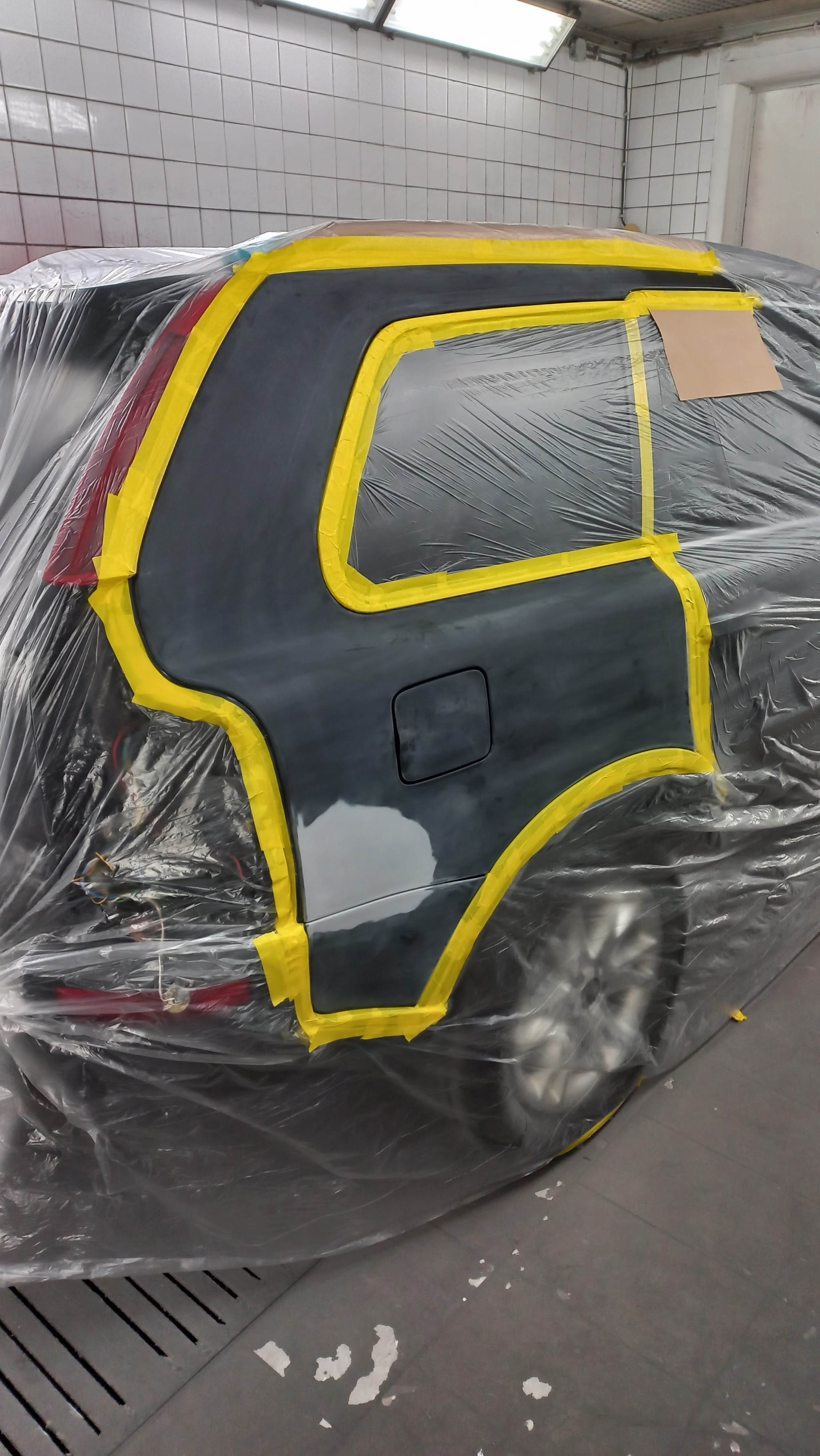 Een auto in de cabine, ingepakt in folie, met het achterscherm uitgeplakt in gele tape