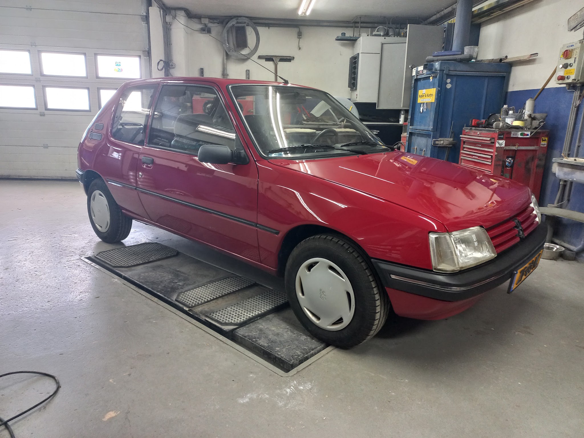 Een rode Peugeot 205 in perfecte staat binnen in de werkplaats