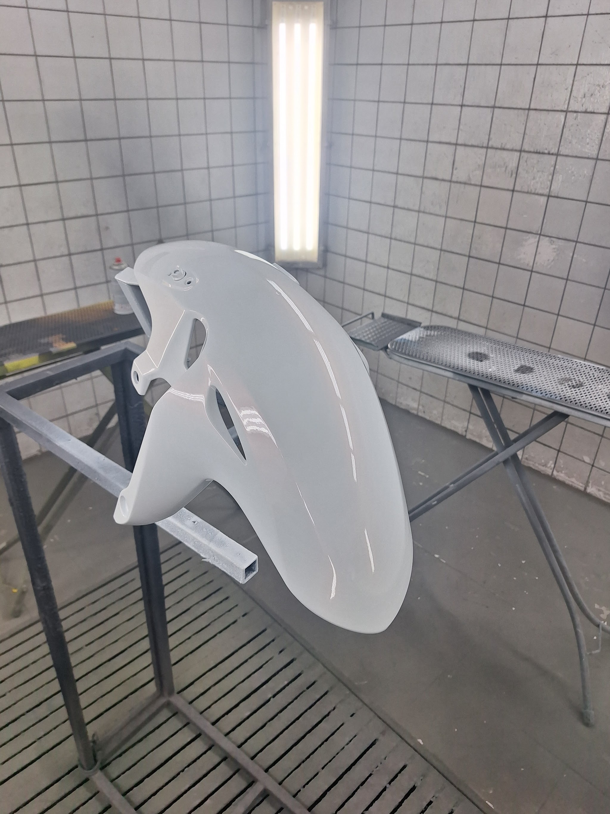 Een wit gespoten spatbord van een motor, hangend aan een standaard in de cabine