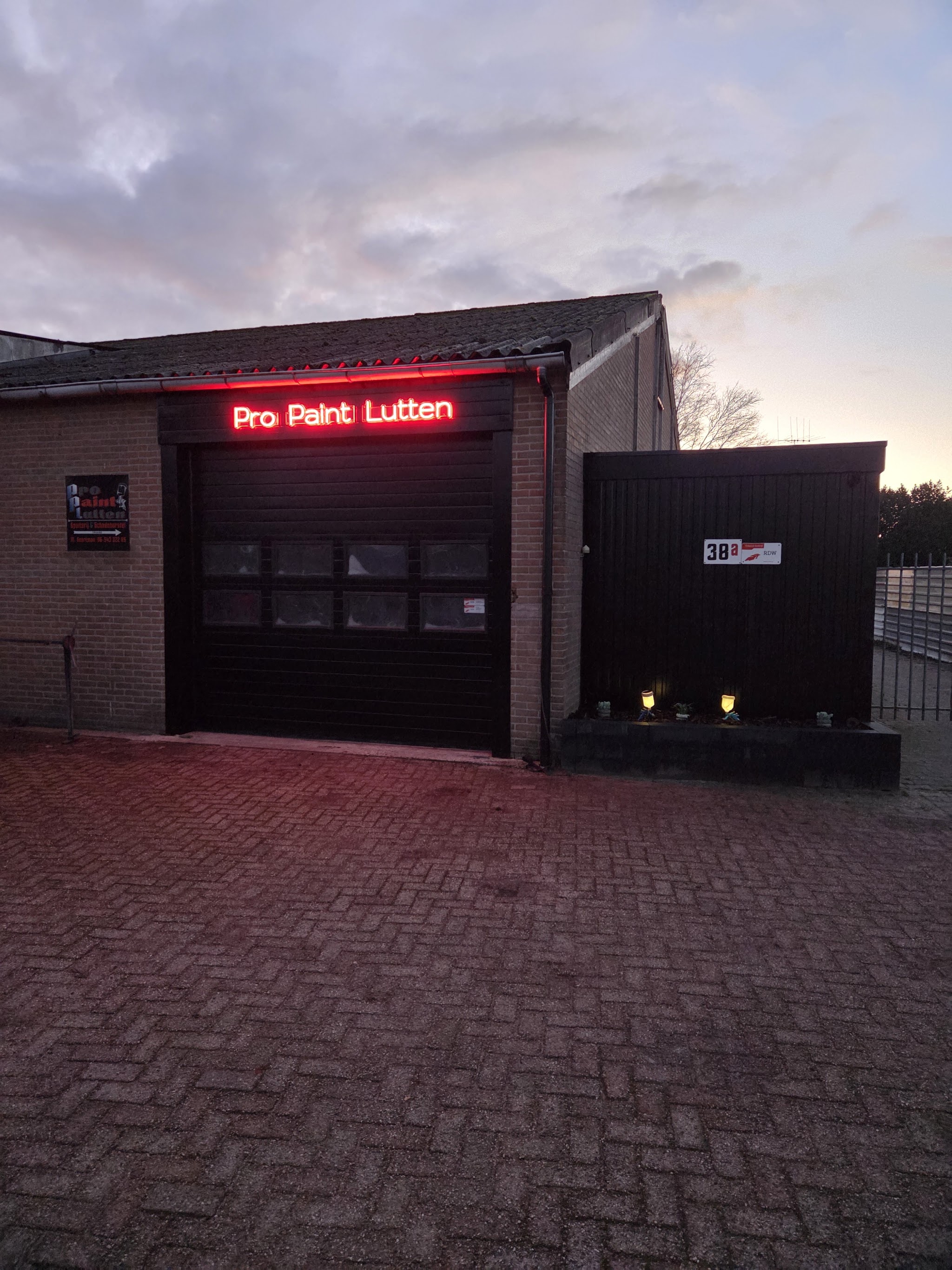 De werkplaats van Pro Paint Lutten aan de Zwarte Dijk bij schemer, met de verlichte naam boven de roldeur