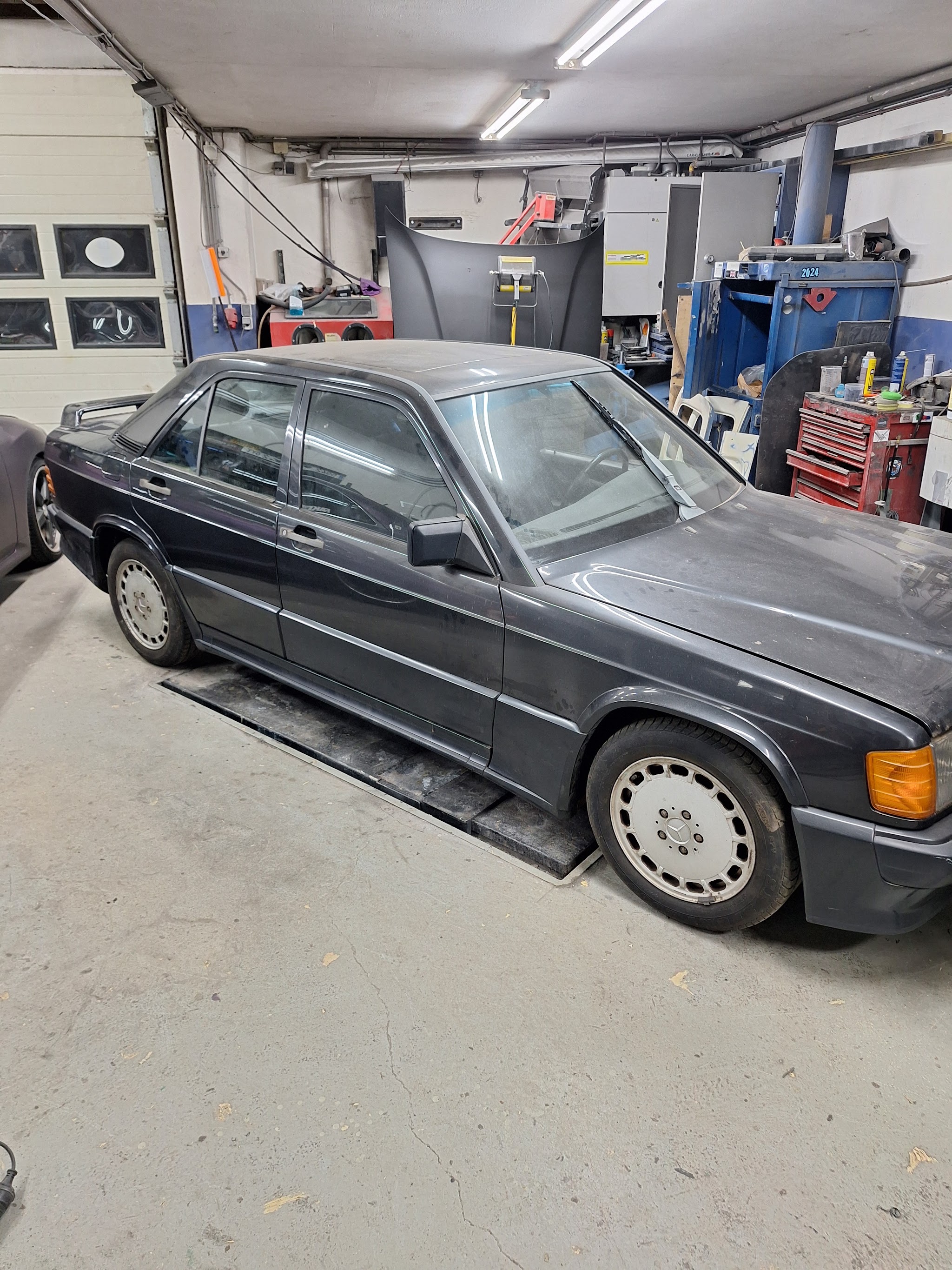 Een Mercedes 190E in de werkplaats, met de menglak en het gereedschap erachter